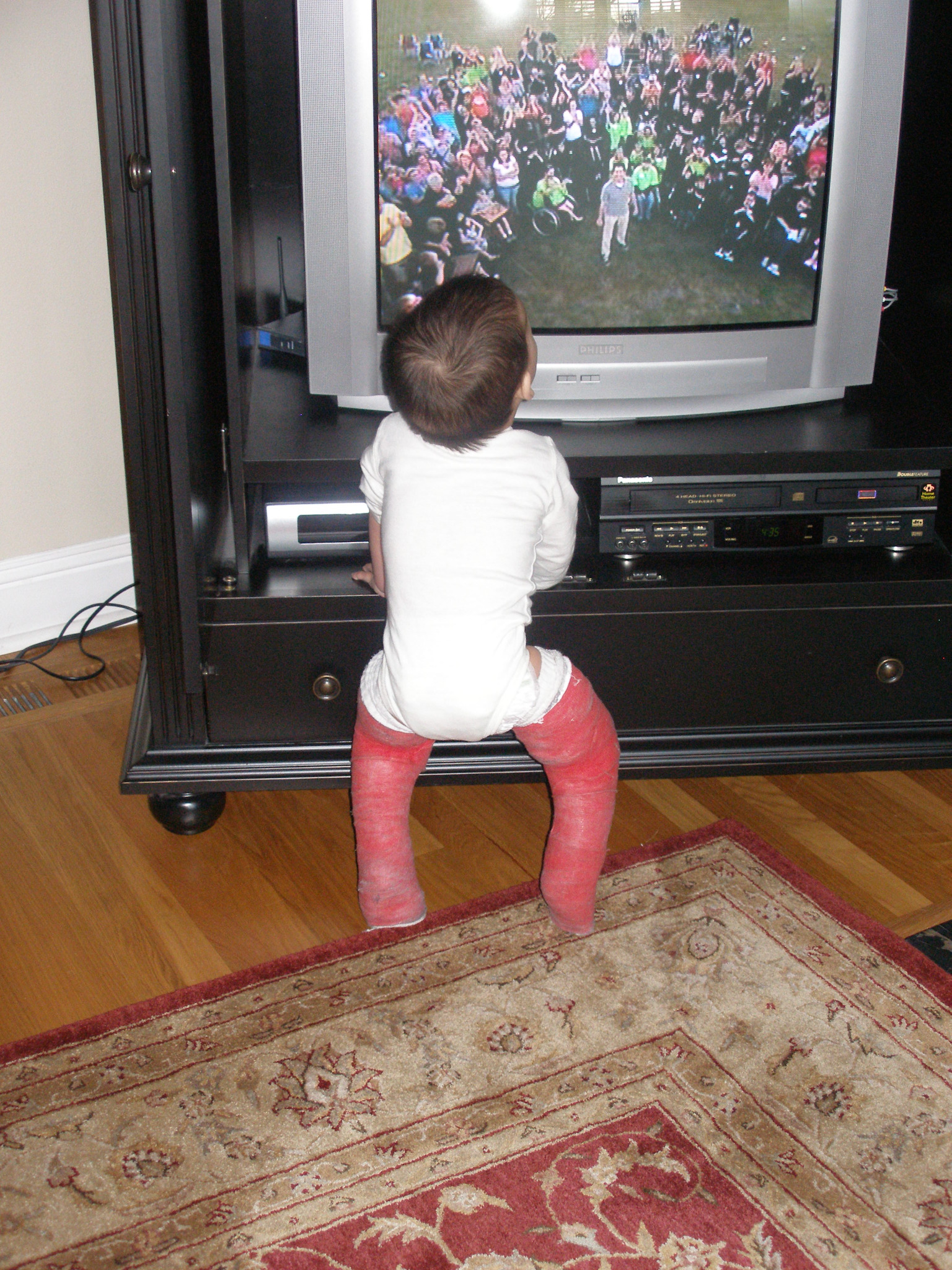 Young child in full-leg casts watching television from behind.